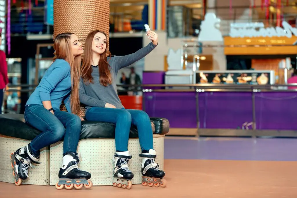 Two girls sitting on a bench with roller blades.